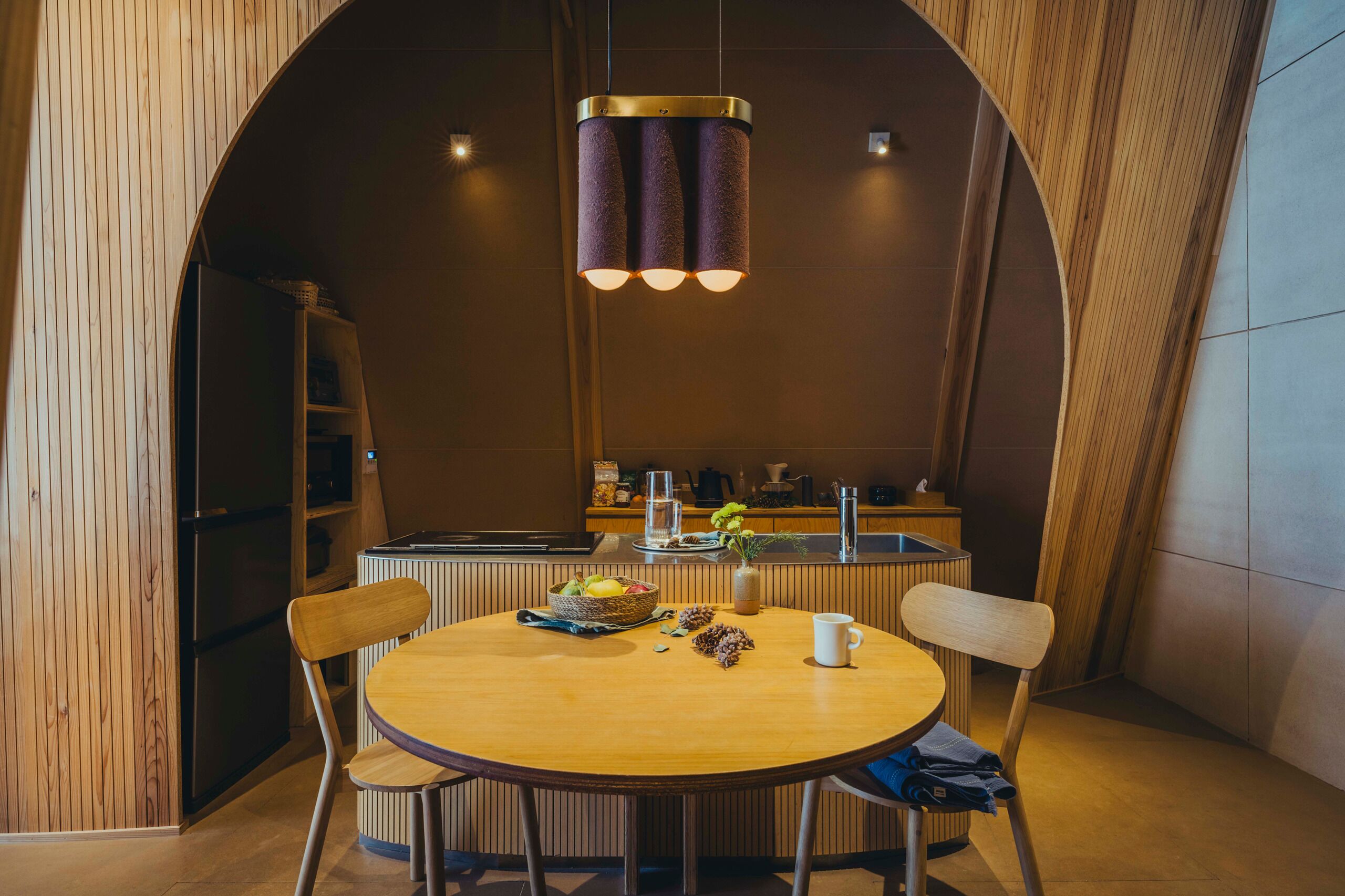 A modern dining area with a round table, two chairs, and a pendant light fixture.