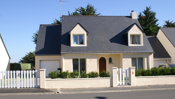 A two-story house with a gabled roof, a front entrance with a wooden door, and a small window on the second floor.