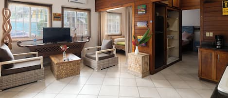 A living room with a television, wicker furniture, a coffee table, and a kitchen area with a refrigerator.