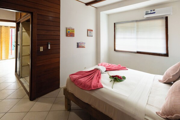 A hotel room with a bed, a window with blinds, a door, and a wall with a thermostat and a sign.