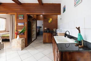 A kitchen with wooden cabinets, a sink, and a countertop. There is a plant on a side table and a sign on the wall.