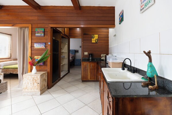A kitchen with wooden cabinets, a sink, and a countertop. There is a plant on a side table and a sign on the wall.