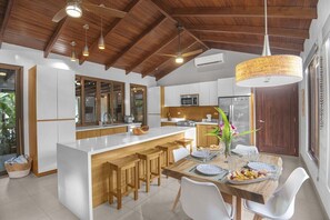 A modern kitchen with a central island, wooden bar stools, and a dining table set for two.