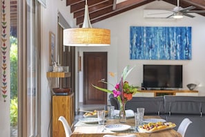 A dining area with a wooden table set for two, a vase with flowers, and a television in the background.