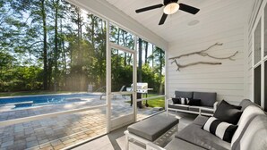 A modern outdoor living space with a pool, a ceiling fan, and a seating area with a sofa and ottoman. - Pawleys Island Retreat with Private Pool (Pawleys Island)