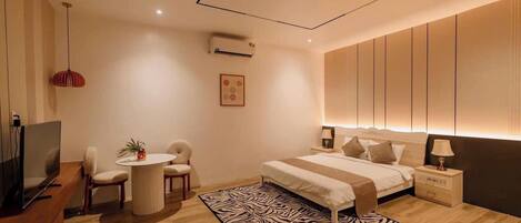 A modern hotel room with a large bed, a desk with a TV, a small round table with chairs, and a zebra-patterned rug.