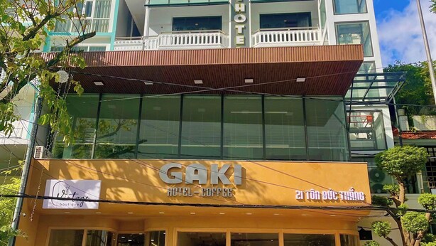 A hotel with a modern facade, a visible sign for 'Gaki Hotel-Coffee', and outdoor seating with umbrellas. - Gaki Hotel (Hue)