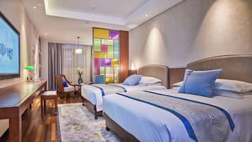 A hotel room with two beds, a desk, a chair, and a large window with curtains.