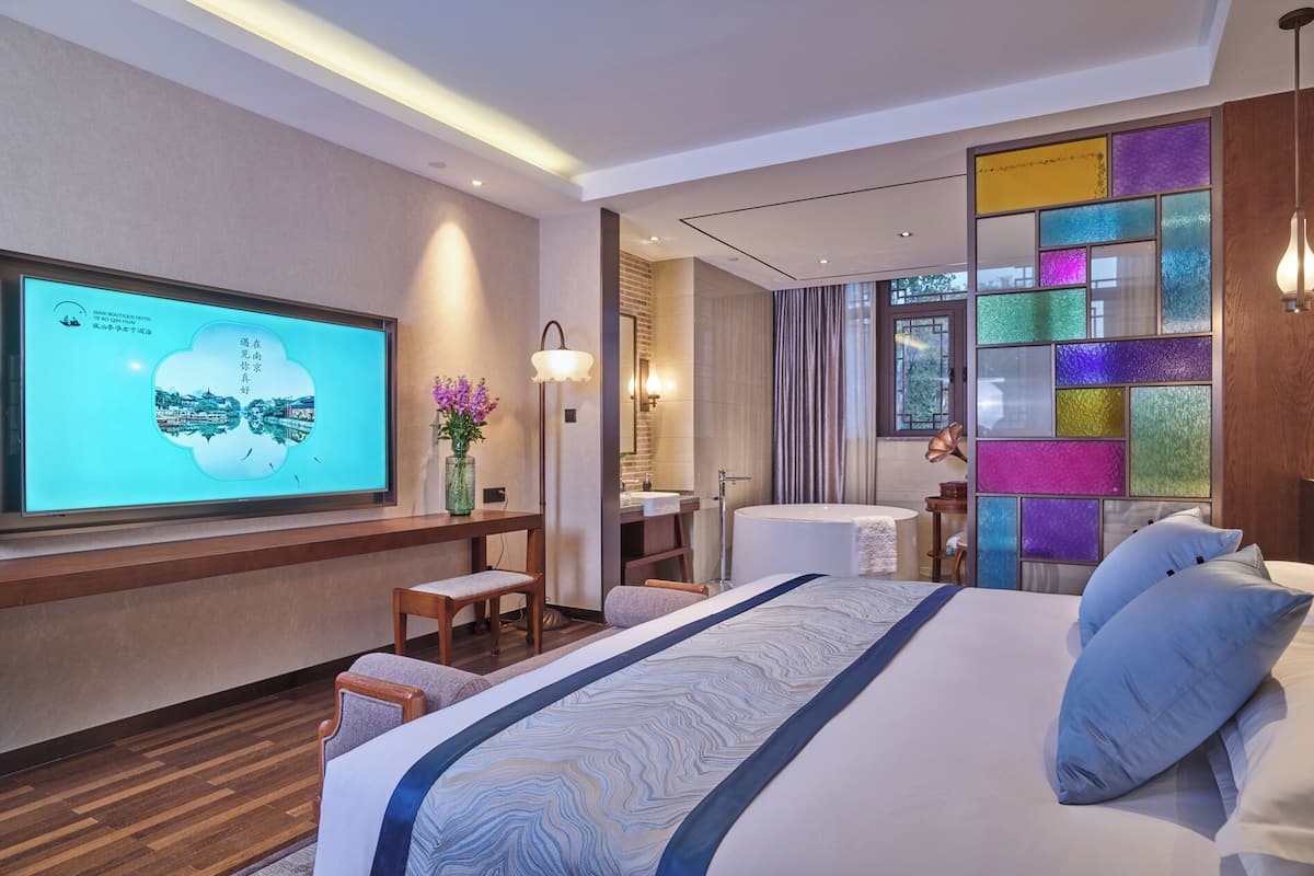 A hotel room with a large bed, a desk with a computer, a bathroom with a bathtub, and a TV displaying a scenic view.