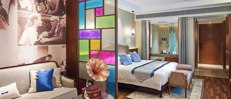 Quarto de hotel moderno com uma cama grande, um sofá, uma mesa redonda e um divisório de parede colorido.