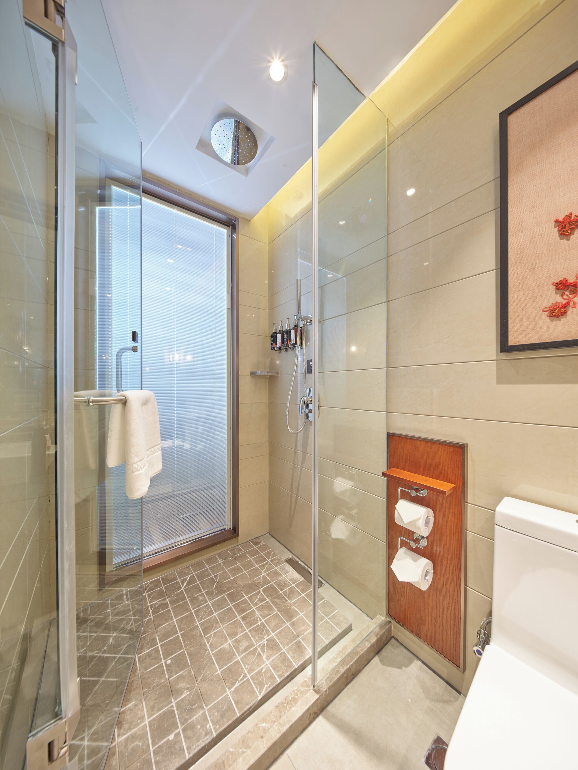 Un baño moderno con mampara de vidrio, inodoro con panel de madera y toallero.