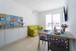 Una cocina moderna con armarios blancos, un sofá verde, una mesa de comedor con sillas y un televisor montado en la pared.