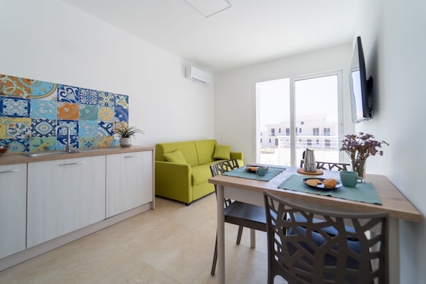 Una cocina moderna con armarios blancos, un sofá verde, una mesa de comedor con sillas y un televisor montado en la pared.