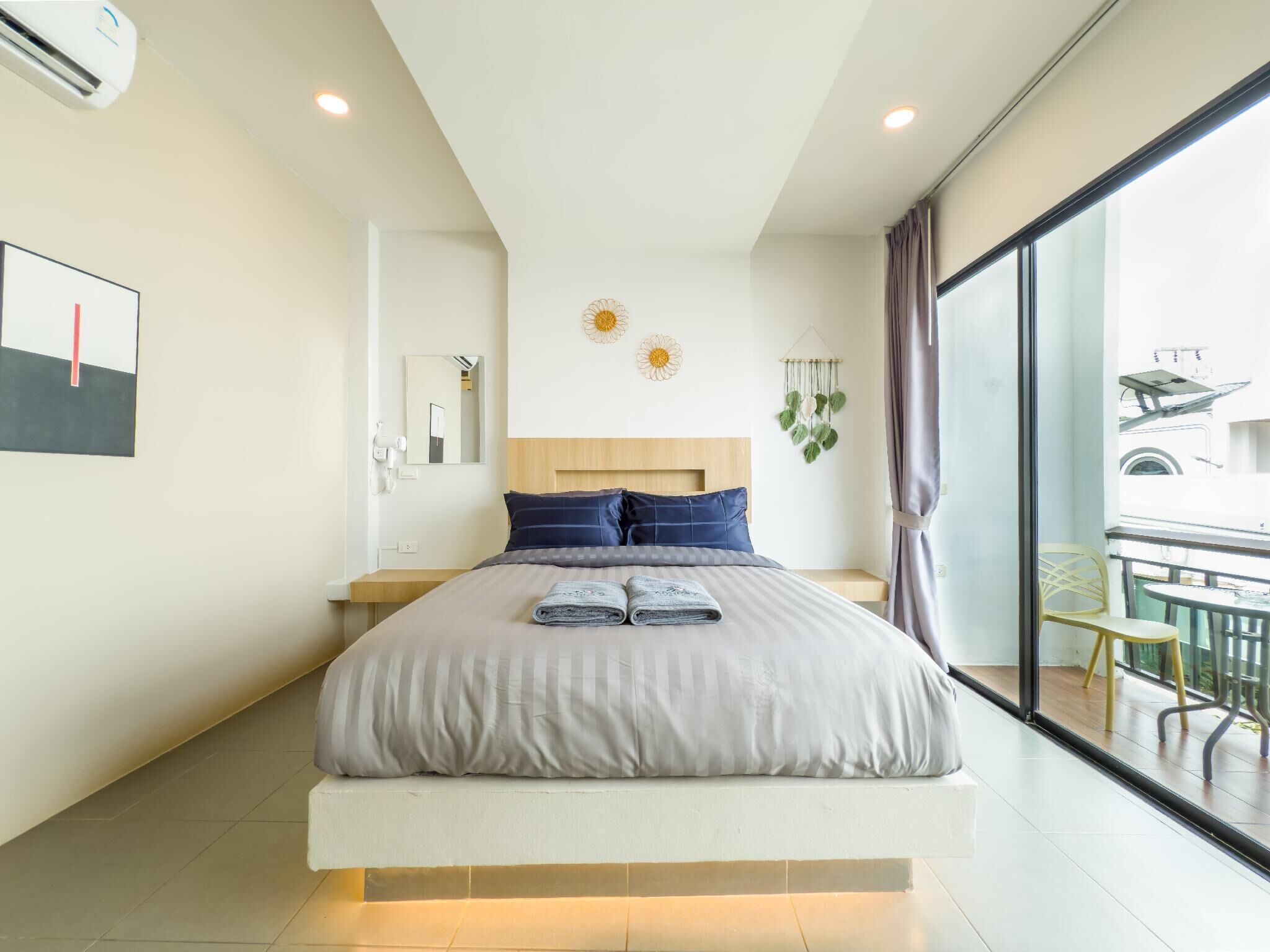 A modern hotel room with a large bed, a bedside table, a mirror, and a view of the outside balcony.