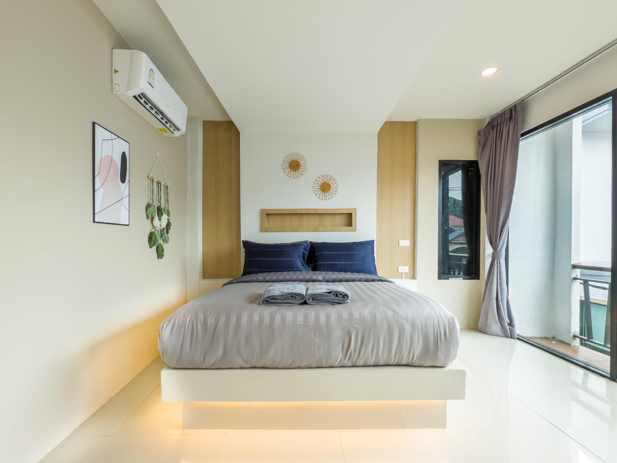 A modern bedroom with a bed, air conditioning unit, artwork, and a window with curtains.