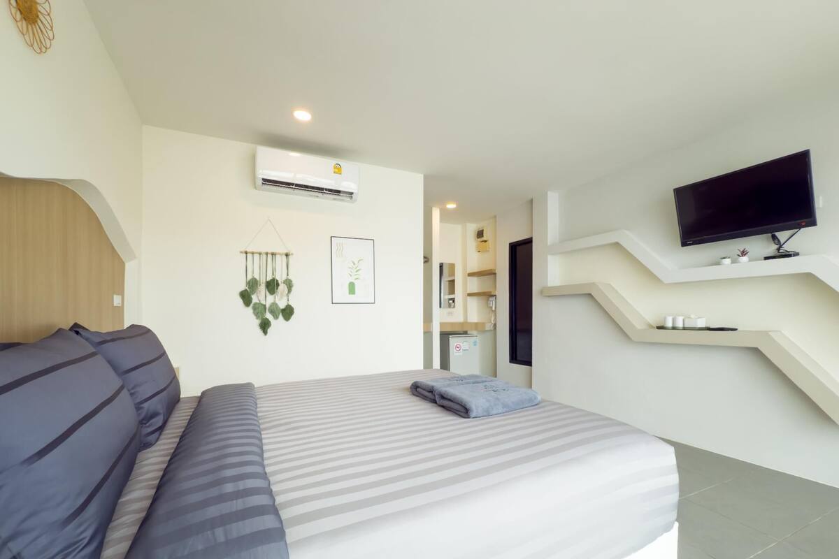 A modern hotel room with a large bed, a mounted TV, and a small kitchenette.