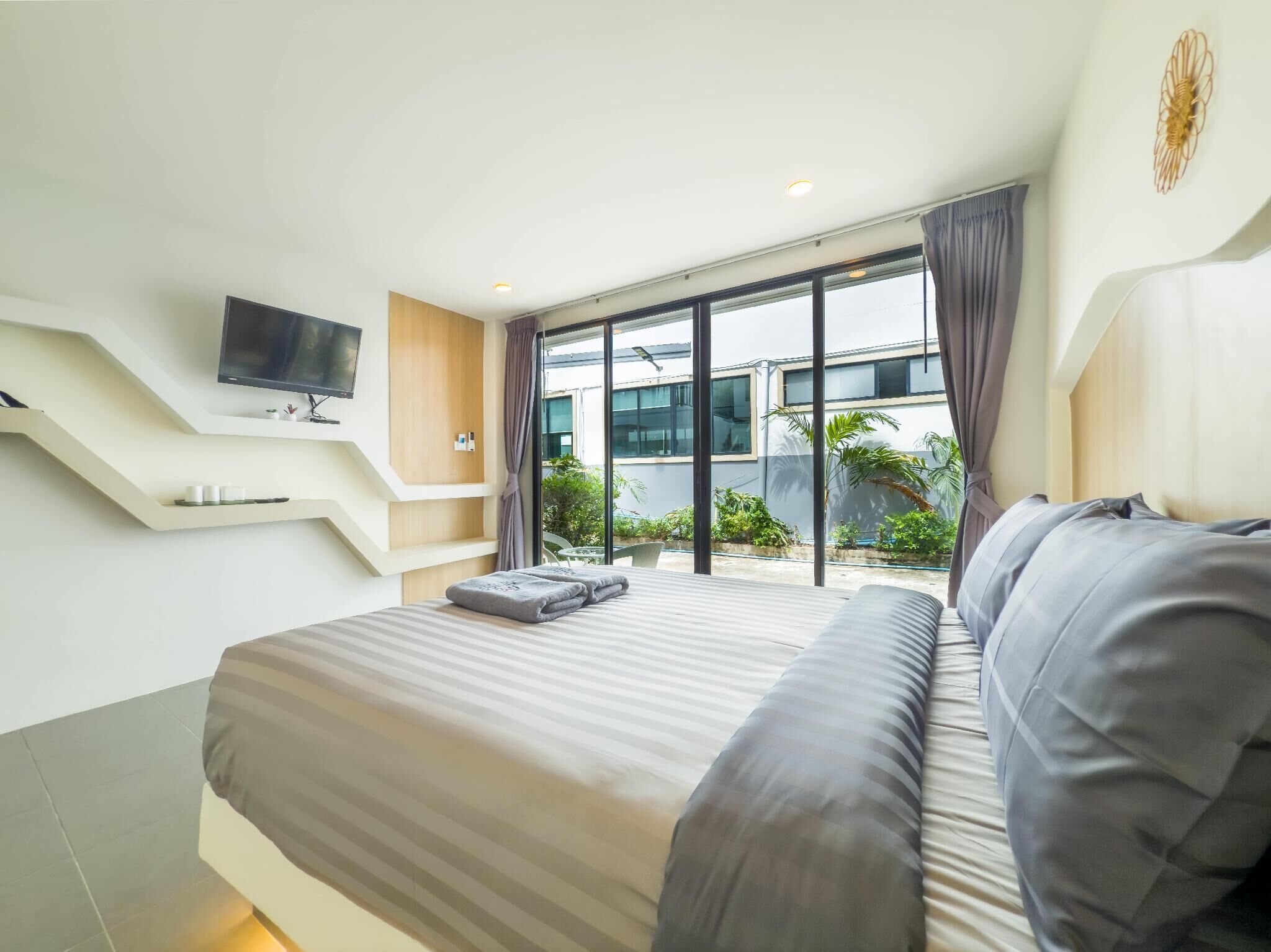 A modern hotel room with a large bed, a flat-screen TV mounted on the wall, and a balcony with a view of the surrounding area.