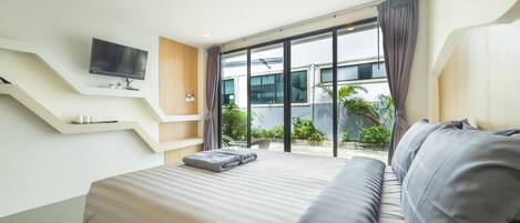 A modern hotel room with a large bed, a flat-screen TV mounted on the wall, and a balcony with a view of the surrounding area.
