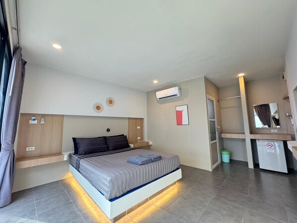 A modern hotel room with a large bed, bedside tables, an air conditioning unit, a small desk, and a mirror.