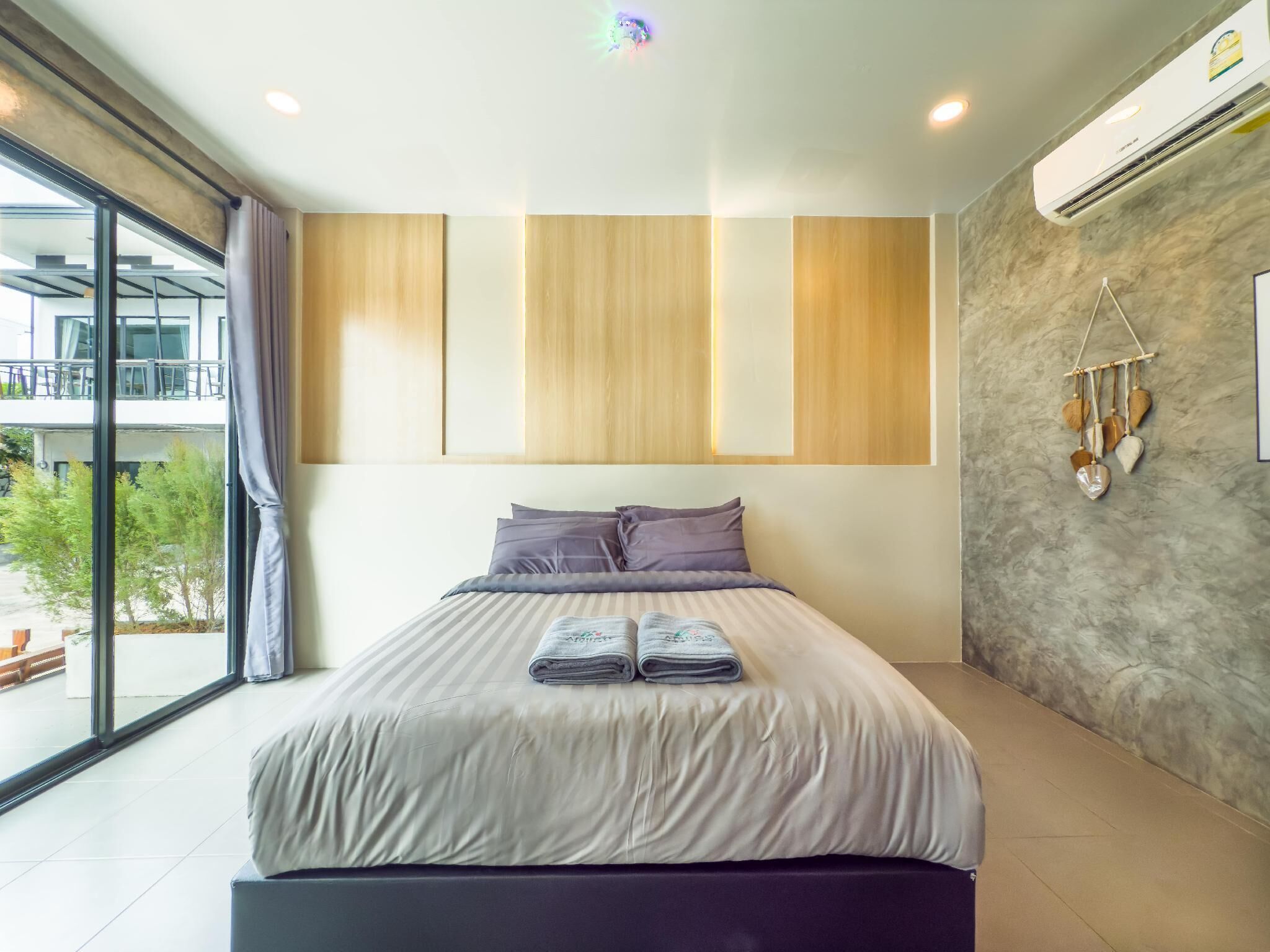 A modern bedroom with a large bed, a view of the outdoors, and a wall-mounted air conditioning unit.