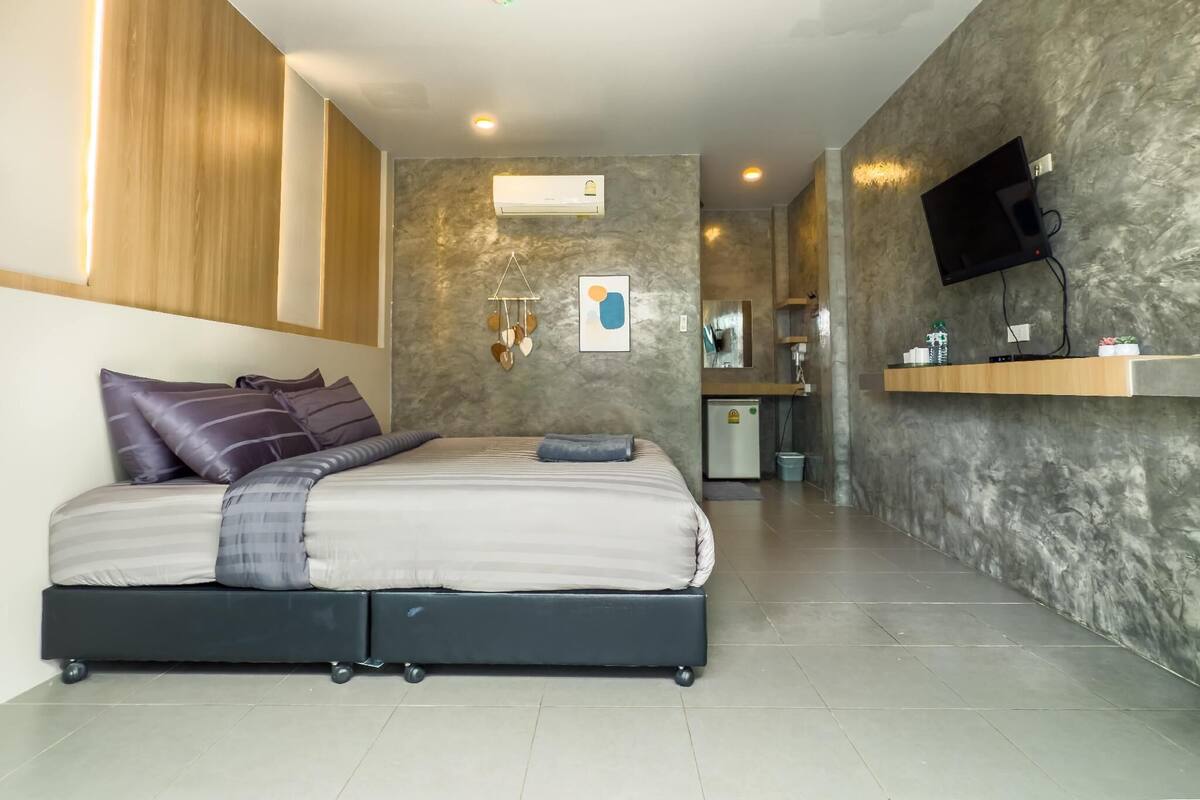 A modern bedroom with a bed, a small kitchenette, and a TV mounted on the wall.