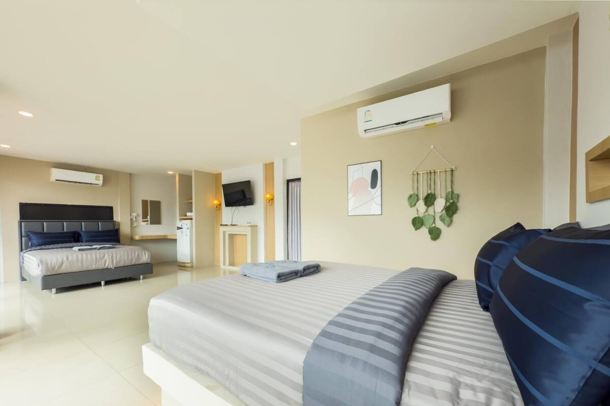 A modern hotel room with a large bed, a TV, an air conditioning unit, and a small kitchenette.