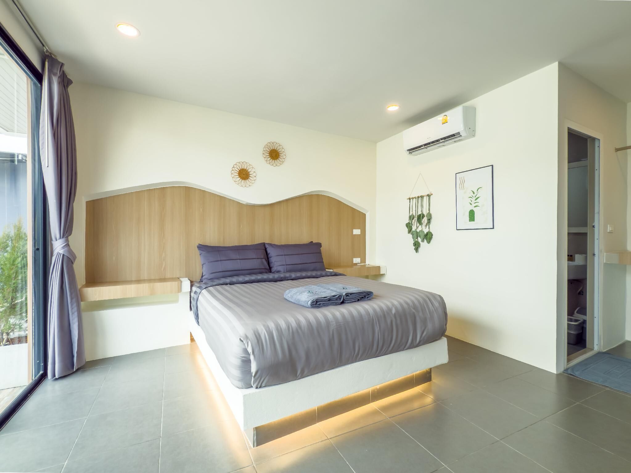 A modern bedroom with a large bed, wooden headboard, and a view of the outdoors.