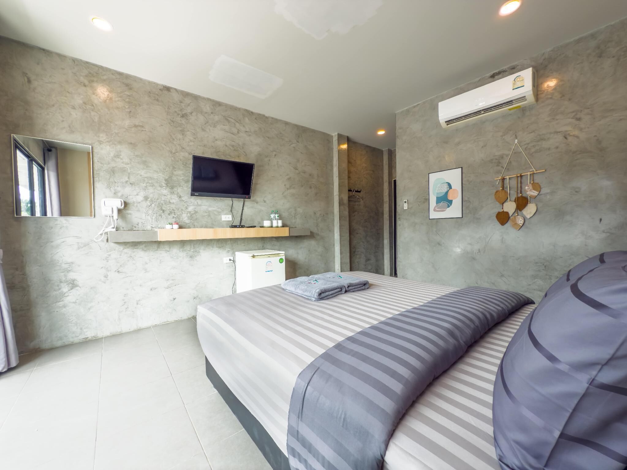 A modern bedroom with a bed, a mounted TV, a small refrigerator, and a wall-mounted air conditioner.
