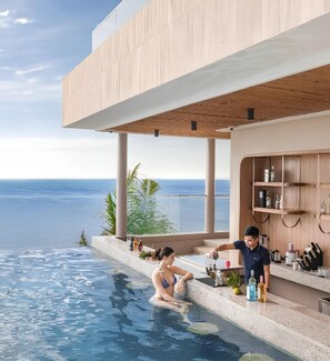 A modern pool area with a view of the ocean, wooden deck, and a bar with various items. - Mandala Oceanfront Driftwood Apartment (Mui Ne)