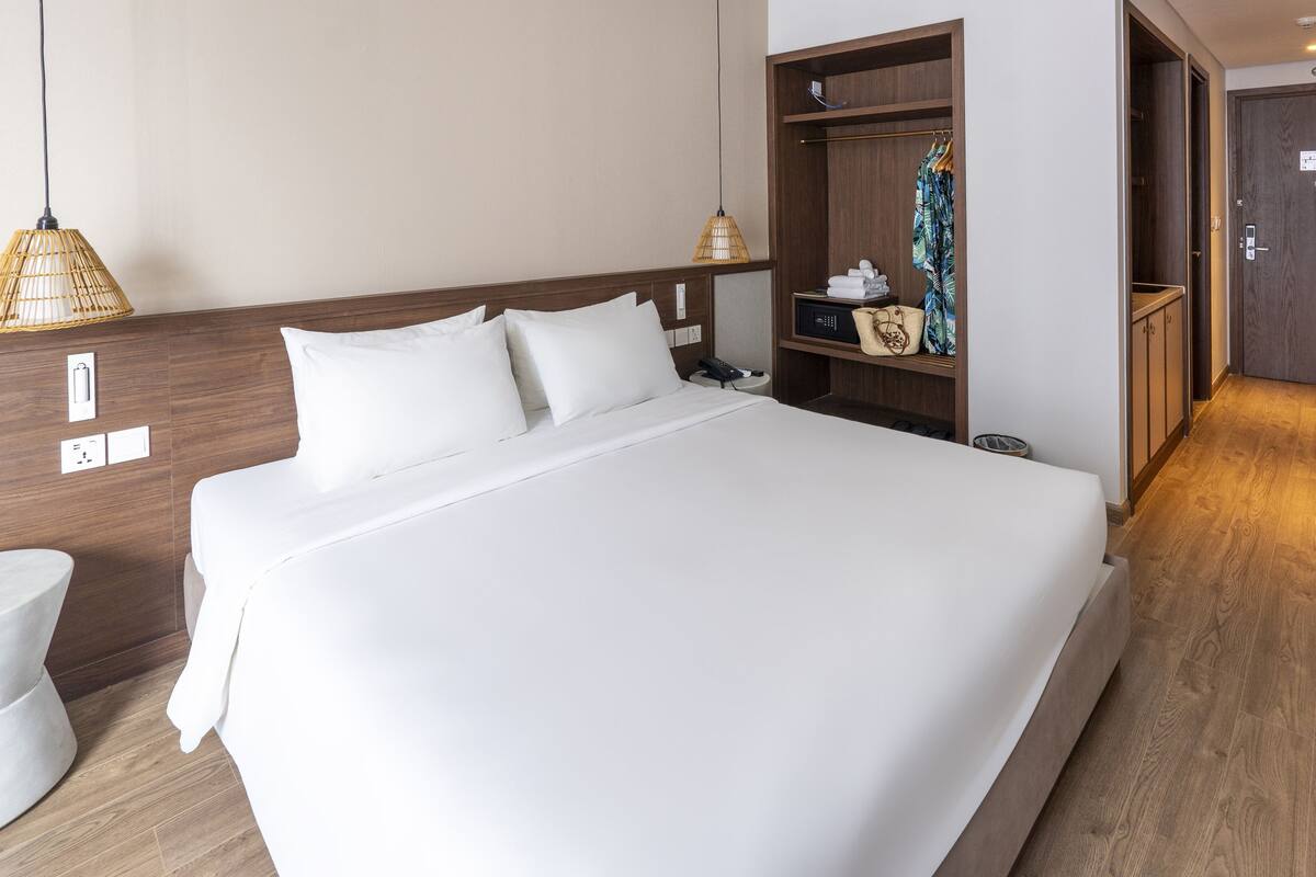 A hotel room with a large bed, wooden headboard, bedside tables, a wardrobe, and a bathroom area.