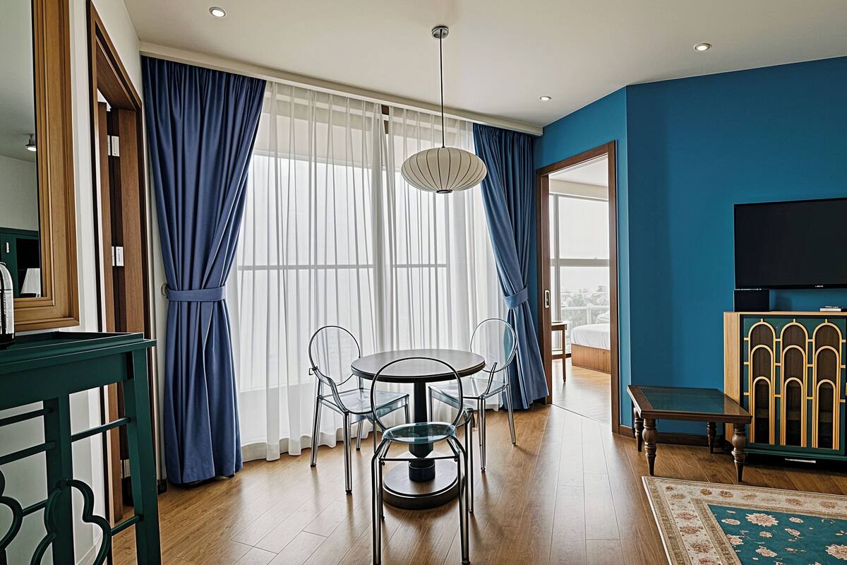 A modern room with a dining table, chairs, a TV, and a large window with curtains.