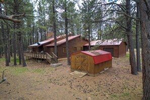 A rustic cabin with a wooden exterior, a red roof, and a small shed. There is a wooden staircase leading to the cabin and a deck area.
