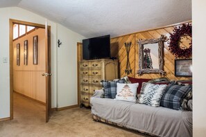 A cozy living room with a wooden wall, a television on a stand, a couch with plaid cushions, and a decorative wreath.
