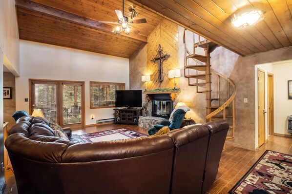 Una sala acogedora con un sofá de cuero, una chimenea, un televisor y una escalera de madera.
