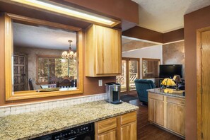 A kitchen with wooden cabinets, a coffee maker, a TV, and a dining area with a chandelier. - Conchas Cabin by Velo (Angel Fire)