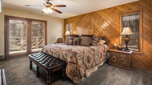 A bedroom with a large bed, a wooden headboard, two bedside lamps, a bench, and a ceiling fan. - Conchas Cabin by Velo (Angel Fire)