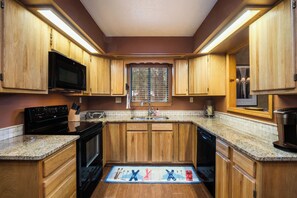 A kitchen with wooden cabinets, a microwave, a stove, and a dishwasher. - Conchas Cabin by Velo (Angel Fire)