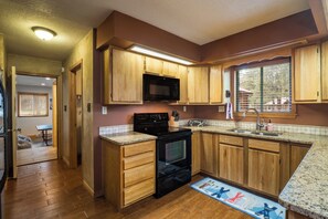 A kitchen with wooden cabinets, a black microwave, and a granite countertop. - Conchas Cabin by Velo (Angel Fire)