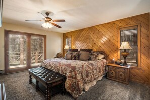 A bedroom with a large bed, a wooden headboard, two bedside lamps, a bench, and a ceiling fan.