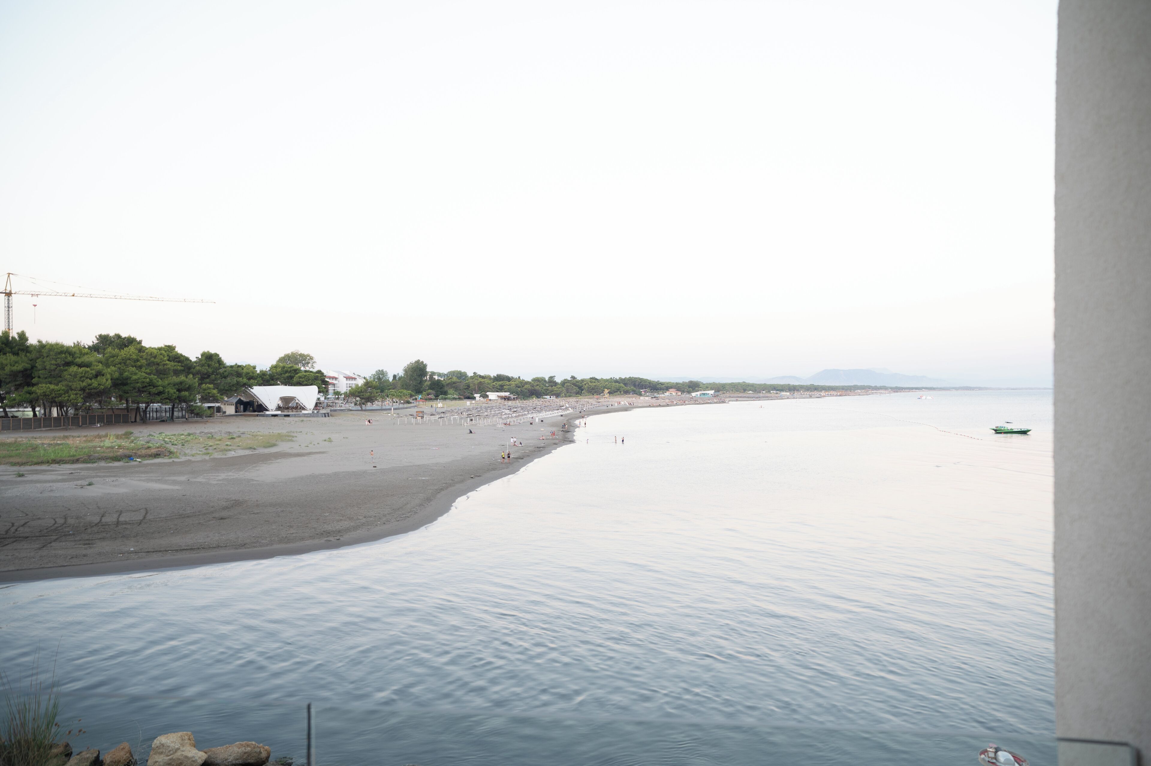 A beach with a calm sea, a few people, and a boat in the distance.