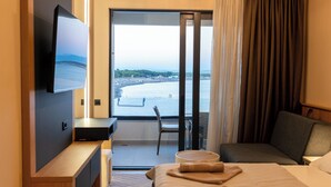 Une chambre d’hôtel comprenant un lit, un bureau, une chaise, une télévision et un balcon avec vue sur la mer.