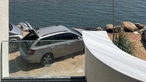 Une vue d’une plage avec une voiture garée au premier plan, un ciel dégagé et une mer calme.