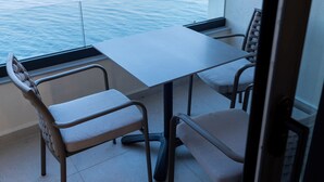 Un balcon avec une table et des chaises, donnant sur une étendue d’eau calme où l’on aperçoit un bateau au loin.