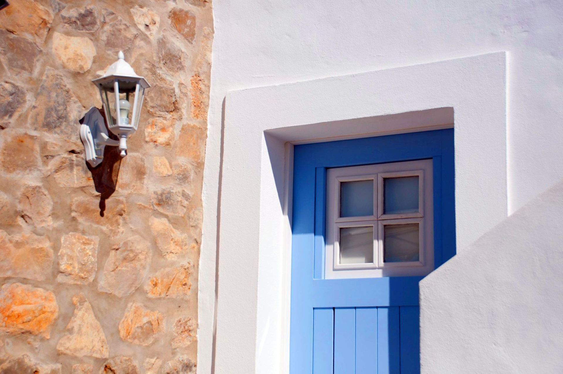 A stone wall with a white wall and a blue door with a window.