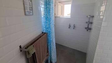 Un baño con paredes de azulejos blancos, una ducha con cortina azul, una ventana y un perchero para toallas.