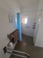 Un baño con paredes de azulejos blancos, una ducha con cortina azul, una ventana y un perchero para toallas.