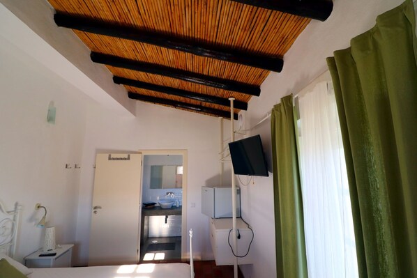 Une chambre d’hôtel avec un plafond en bois, un lit, un bureau avec une lampe, un téléviseur fixé au mur et une salle de bain visible à travers une porte ouverte.