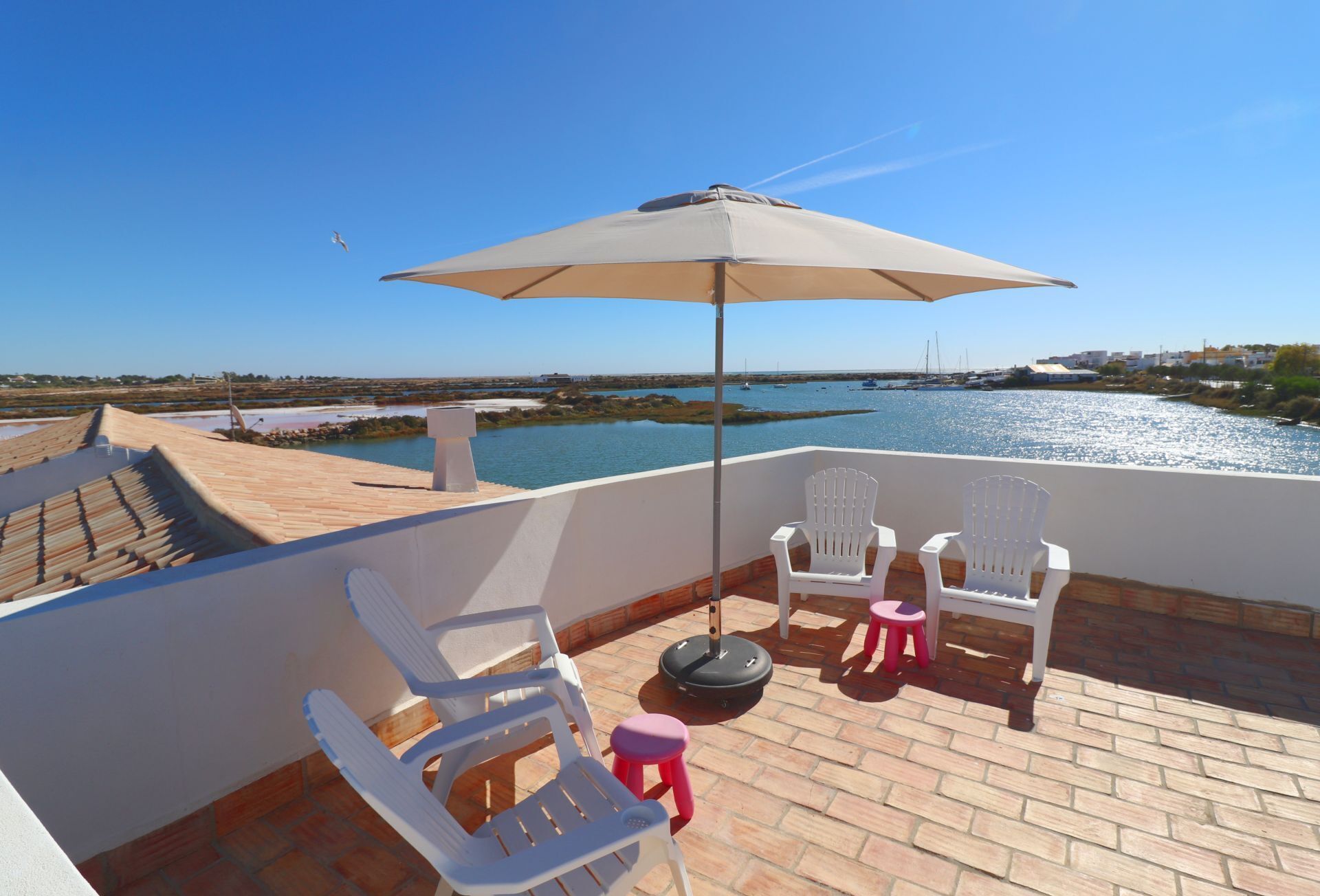 Een terras met twee witte stoelen en een tafel, een parasol en uitzicht op een waterpartij en verre gebouwen.