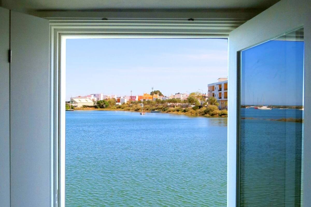 A view from a balcony with a railing, overlooking a body of water and buildings in the distance.
