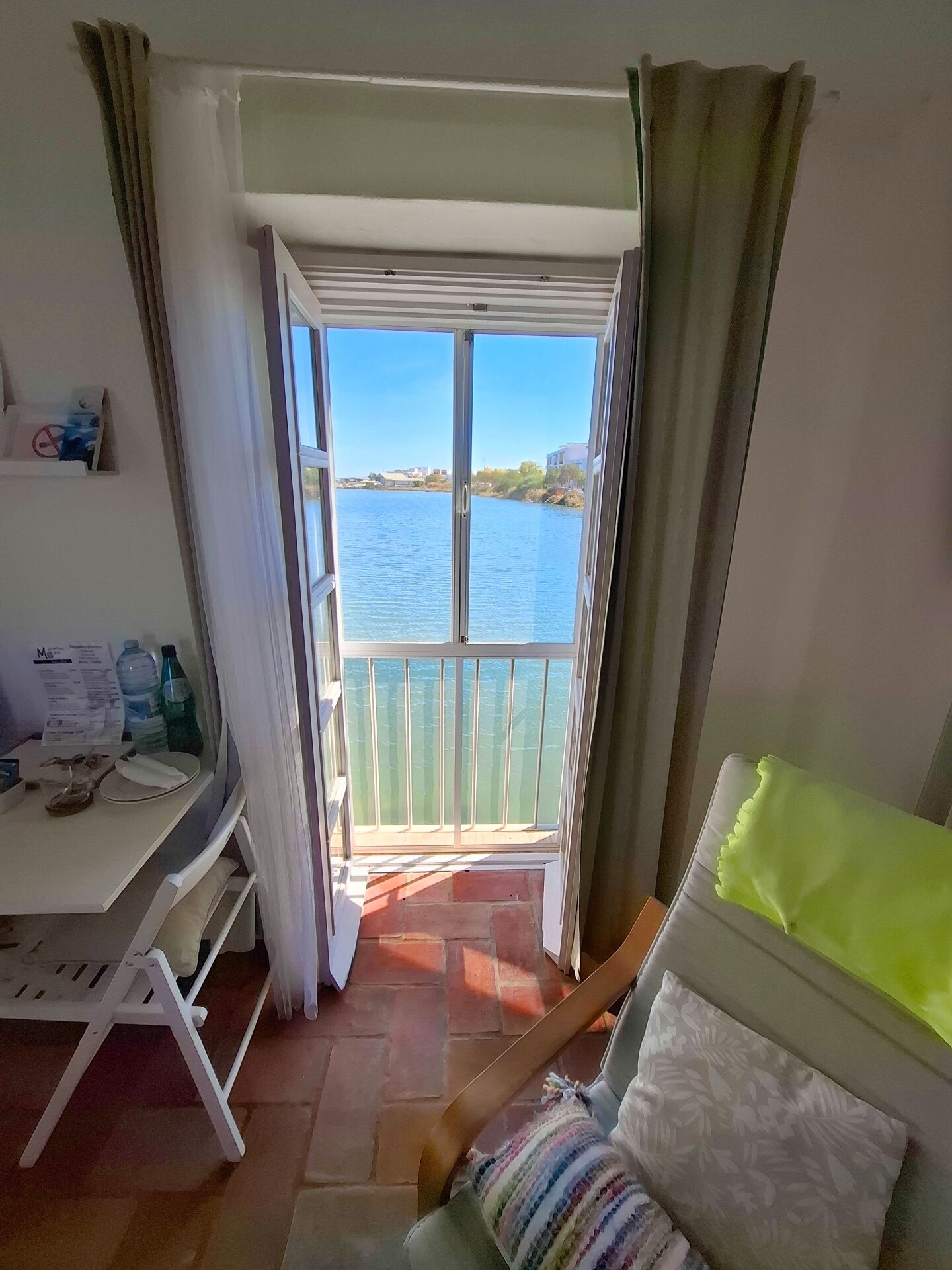 Una stanza con un balcone affacciato sull'acqua, una scrivania con sedia e un letto con copriletto verde.